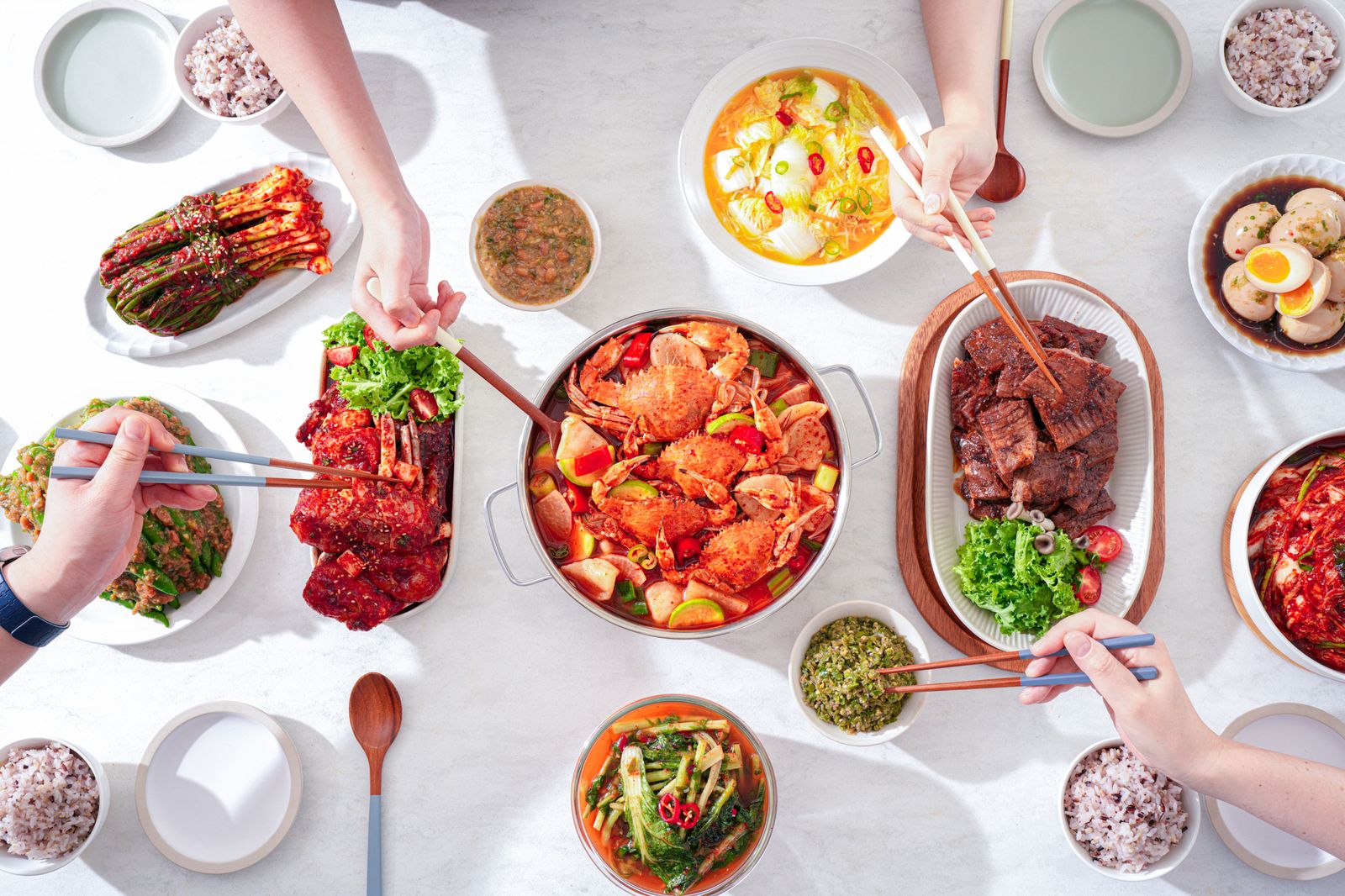 여러 사람이 젓가락으로 함께 나누는 한식 상차림을 위에서 내려다본 음식 사진
